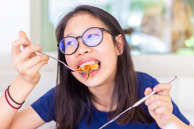 Giovane adolescente femminile con apparecchi ortodontici mangiare e mordere la sua pizza