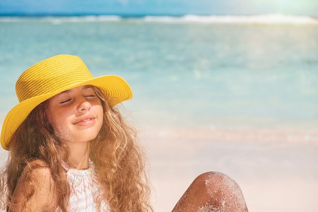 Giovane adolescente in bikini e cappello giallo. Bella ragazza con i capelli lunghi in un cappello giallo in riva all'oceano. Vacanze estive e concetto di viaggio