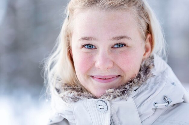 Giovane adolescente sorridente in un parco innevato Bionda carina con una giacca bianca Camminare all'aria aperta in inverno e nelle stagioni fredde Primo piano