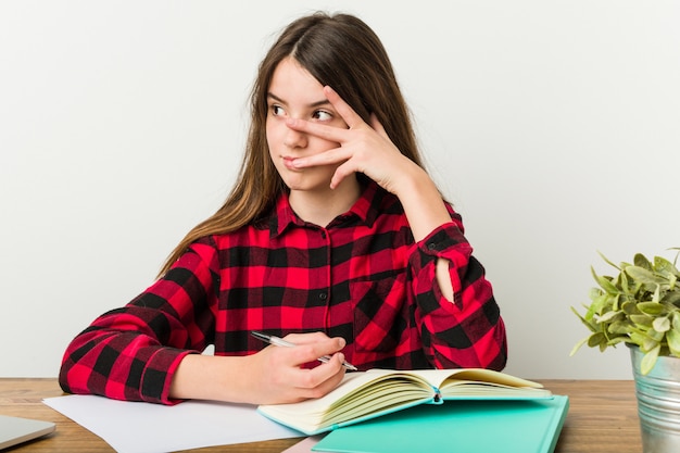 Giovane adolescente tornando alla sua routine facendo i compiti battito di ciglia alla telecamera attraverso le dita