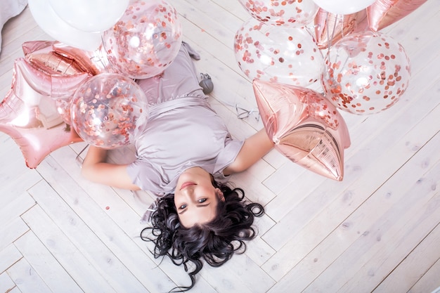 giovane adulto bella donna in abito da festa alla moda con palloncini rosa sdraiato sul pavimento di legno