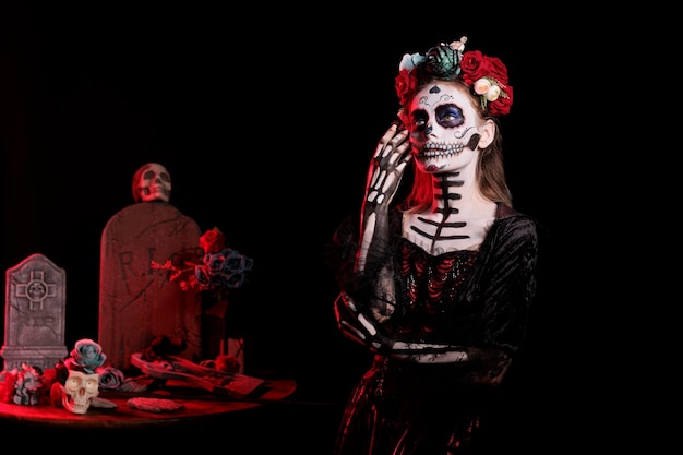 Giovane adulto che agisce in modo affascinante come dea dei morti in studio, indossa una corona di fiori e un costume nero di Halloween. Raffigurante santa muerte o la cavalera catrina, trucco rituale.