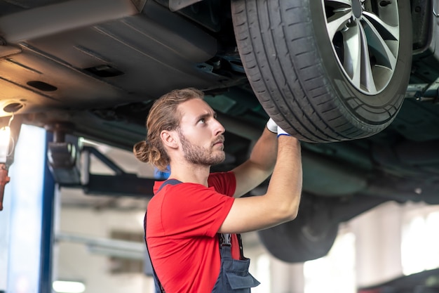 Giovane adulto fiducioso uomo in uniforme da lavoro lavorando su automobili