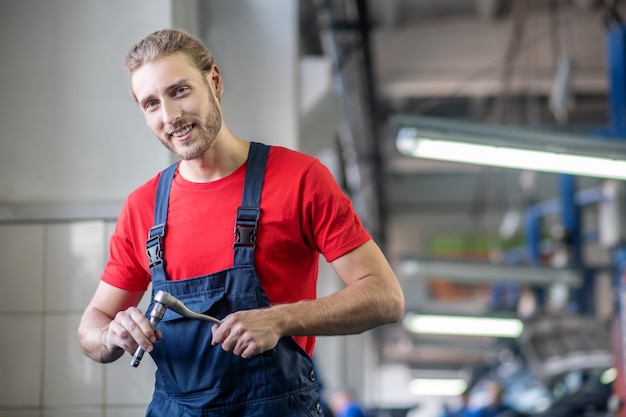 Giovane adulto fiducioso uomo in uniforme da lavoro lavorando su automobili