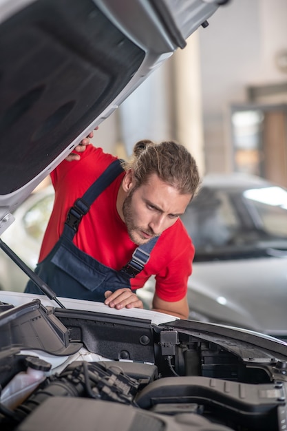 Giovane adulto fiducioso uomo in uniforme da lavoro lavorando su automobili