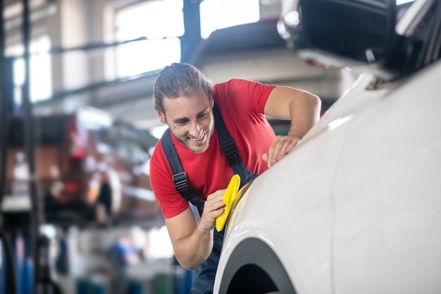 Giovane adulto fiducioso uomo in uniforme da lavoro lavorando su automobili