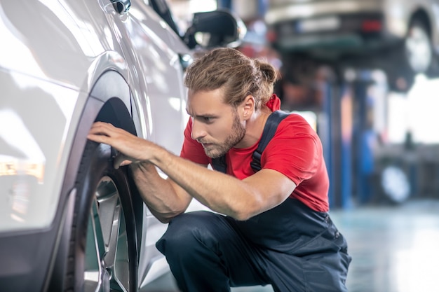 Giovane adulto fiducioso uomo in uniforme da lavoro lavorando su automobili