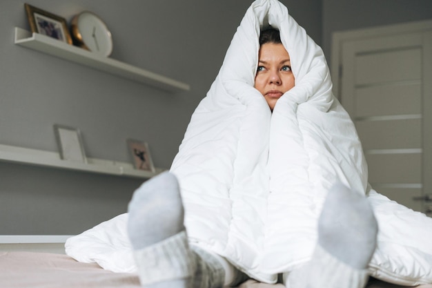 Giovane adulto infelice donna solitaria quarant'anni plus size corpo positivo in grande coperta bianca sul letto di casa