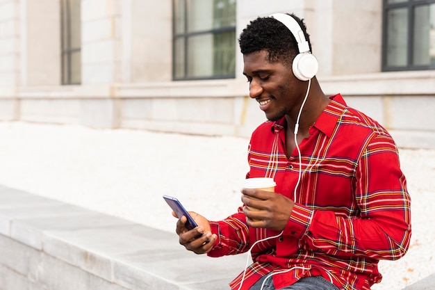 Giovane adulto maschio utilizzando il suo telefono cellulare bianco bere il suo caffè