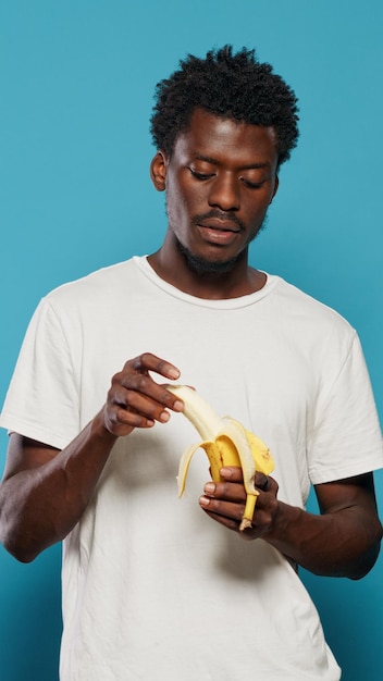 Giovane adulto sbucciare banana, preparando a mangiare frutta per le vitamine. Uomo spensierato che presenta uno spuntino vegetariano giallo alla telecamera, pubblicizzando una sana alimentazione naturale e una dieta. Adulti che mangiano