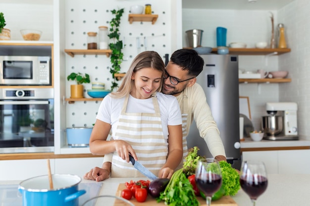 Giovane affettuoso che bacia sua moglie mentre sta facendo colazione Bella giovane coppia sta parlando e sorridendo mentre cucina cibo sano in cucina a casaL'uomo sta baciando la sua ragazza sulla guancia