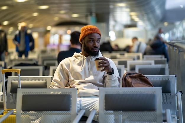 Giovane africano che beve caffè e mangia un panino mentre aspetta di volare al terminal dell'aeroporto