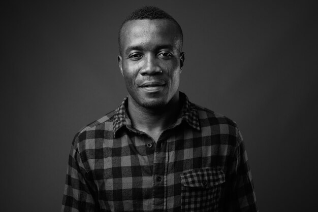 giovane africano che indossa la camicia a scacchi contro il muro grigio. bianco e nero