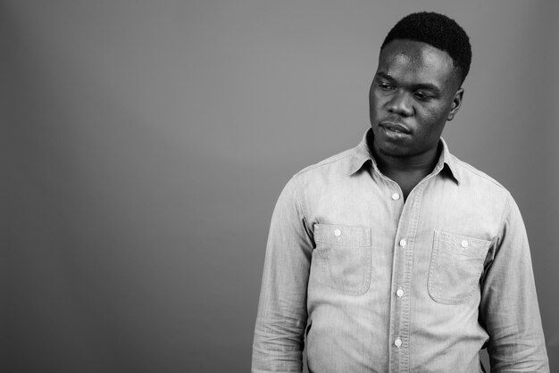 giovane africano che indossa la camicia di jeans contro il muro grigio. bianco e nero