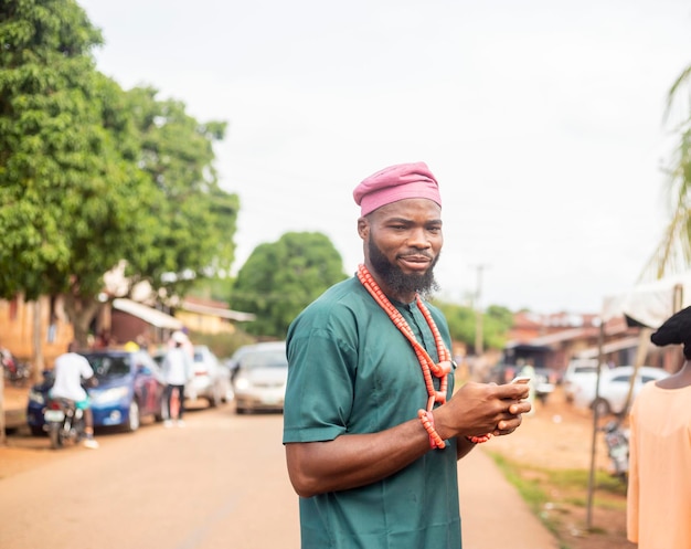 Giovane africano guardando mobile a portata di mano in piedi al di fuori di una strada rurale