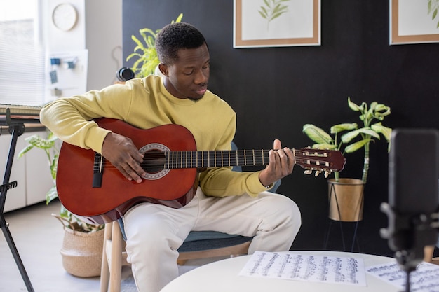 Giovane africano serio che suona la chitarra davanti alla fotocamera dello smartphone