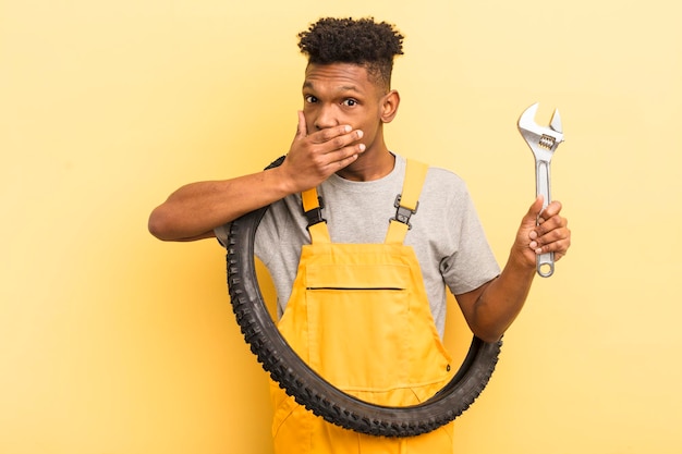 Giovane afro nero che copre la bocca con le mani con un concetto meccanico di bicicletta scioccato