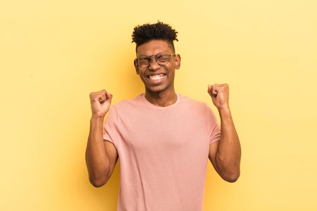 Giovane afro nero che sembra estremamente felice e sorpreso che celebra il successo gridando e saltando