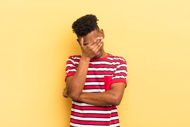 Giovane afro nero che sembra imbarazzato o arrabbiato con un mal di testa che copre il viso con la mano