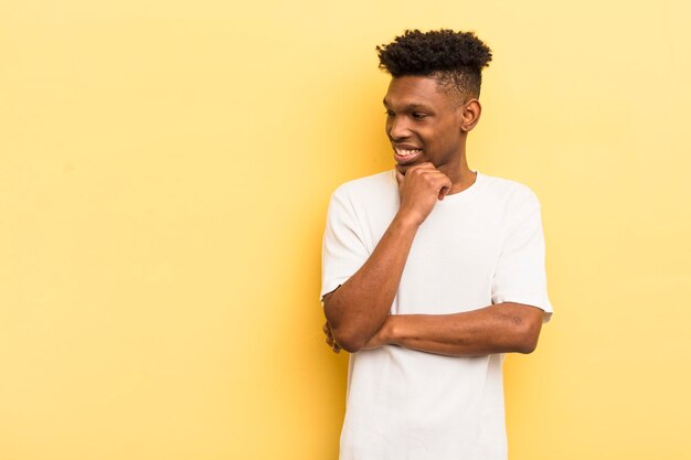 Giovane afro nero che sorride con un'espressione felice e sicura con la mano sul mento con uno spazio di copia a lato