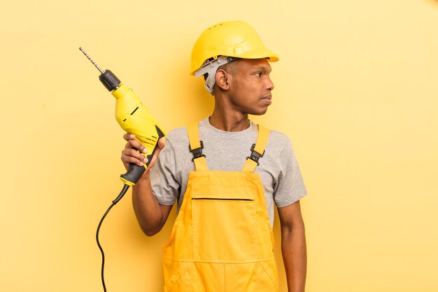 Giovane afro nero su vista profilo pensando immaginando o sognando ad occhi aperti lavoratore domestico con un trapano