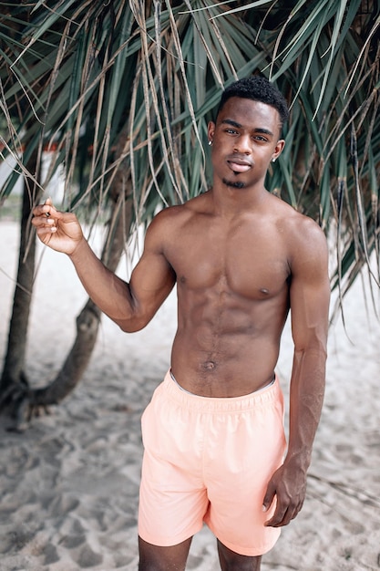 Giovane afroamericano che si rilassa sulla spiaggia vicino alle palme Modello maschile a torso nudo che prende il sole. Swaggy C in vacanza. Phuket.