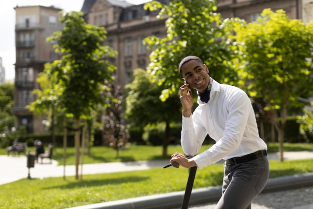 Giovane afroamericano che usa il telefono cellulare mentre è in piedi con uno scooter elettrico su una strada