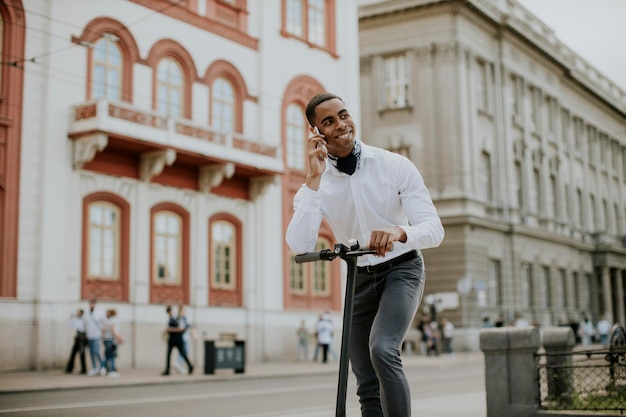 Giovane afroamericano che usa il telefono cellulare mentre è in piedi con uno scooter elettrico su una strada