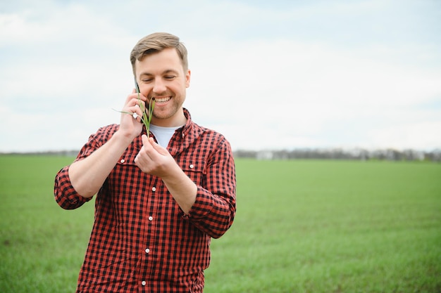 Giovane agricoltore bello che cammina su terreni agricoli e parla al cellulare