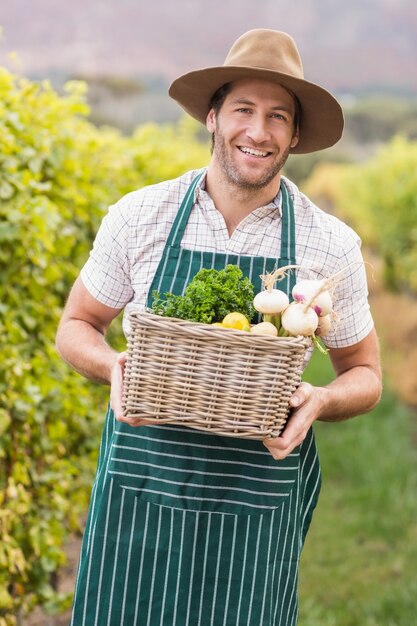 Giovane agricoltore felice che tiene un cestino di verdure