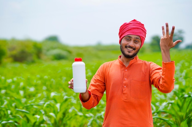 Giovane agricoltore indiano che mostra la bottiglia di fertilizzante liquido al campo agricolo.