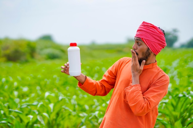 Giovane agricoltore indiano che mostra la bottiglia di fertilizzante liquido al campo agricolo.