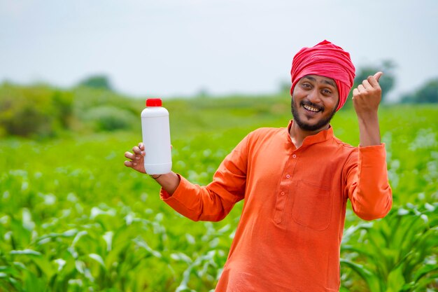 Giovane agricoltore indiano che mostra la bottiglia di fertilizzante liquido al campo agricolo.