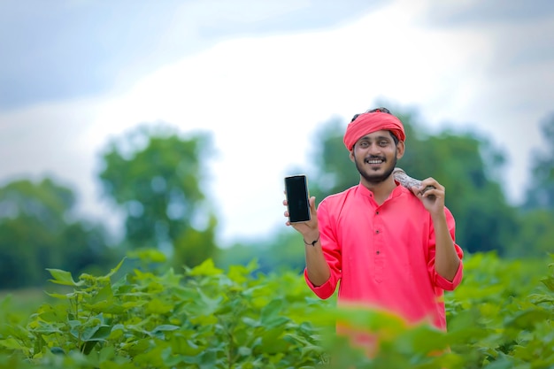 Giovane agricoltore indiano che mostra smartphone nel campo di cotone verde