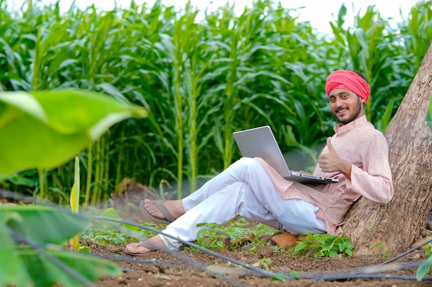 Giovane agricoltore indiano che utilizza computer portatile al campo di agricoltura.