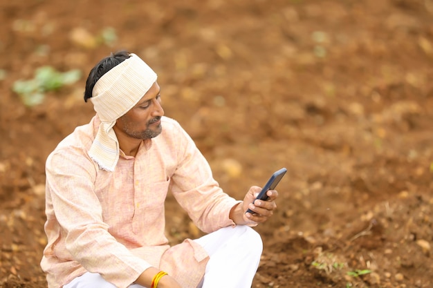 Giovane agricoltore indiano che utilizza smartphone al campo agricolo.