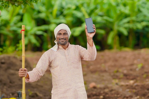 Giovane agricoltore indiano che utilizza smartphone al campo agricolo.