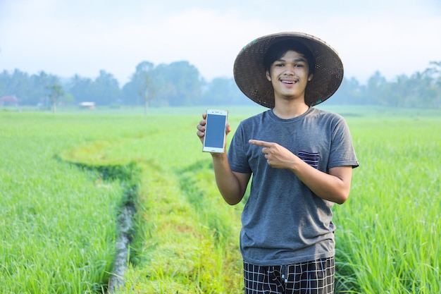 Giovane agricoltore intelligente millenario che dirige il dito sullo smartphone con schermo vuoto nel mezzo del campo di riso
