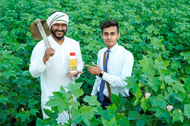 Giovane agronomista indiano che dà una bottiglia di fertilizzante liquido a un contadino in un campo di agricoltura verde