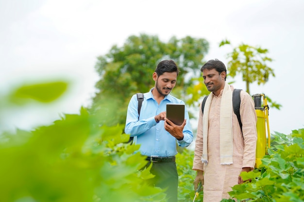 Giovane agronomo indiano che mostra alcune informazioni all'agricoltore in tablet al campo agricolo.