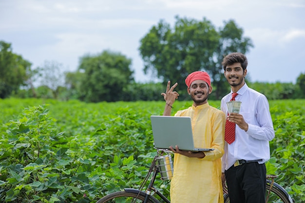 Giovane agronomo indiano che mostra alcune informazioni all'agricoltore nel computer portatile al campo di cotone