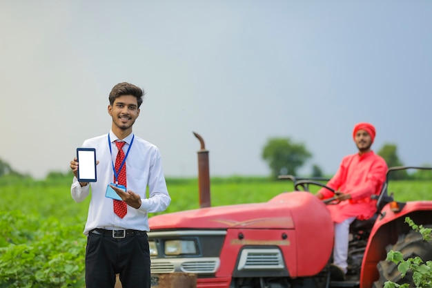 Giovane agronomo indiano che mostra smartphone o tablet al campo