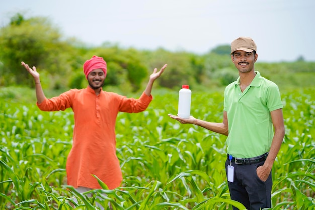 Giovane agronomo indiano che tiene in mano una bottiglia di fertilizzante liquido con agricoltore al campo agricolo verde.