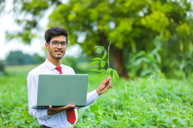 Giovane agronomo indiano con il computer portatile al campo