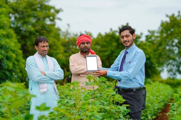 Giovane agronomo indiano o banchiere che mostra tablet con gli agricoltori al campo agricolo.