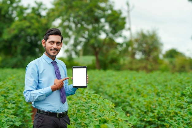 Giovane agronomo indiano o ufficiale che mostra tablet al campo agricolo.