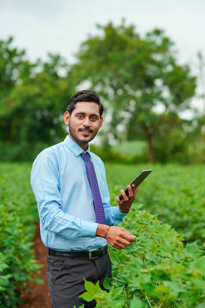 Giovane agronomo indiano o ufficiale che utilizza tablet al campo agricolo.