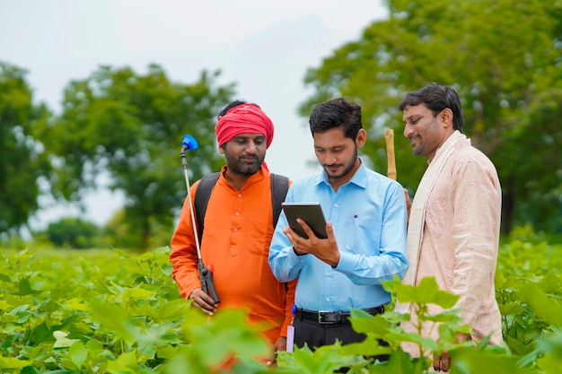 Giovane agronomo o banchiere indiano che mostra alcune informazioni all'agricoltore in tablet al campo agricolo.
