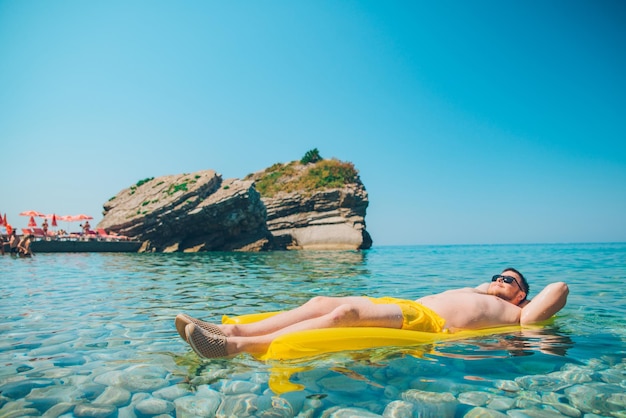 Giovane al materasso gonfiabile giallo in chiara acqua trasparente