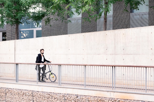 Giovane alla moda che cammina per la città con una bicicletta